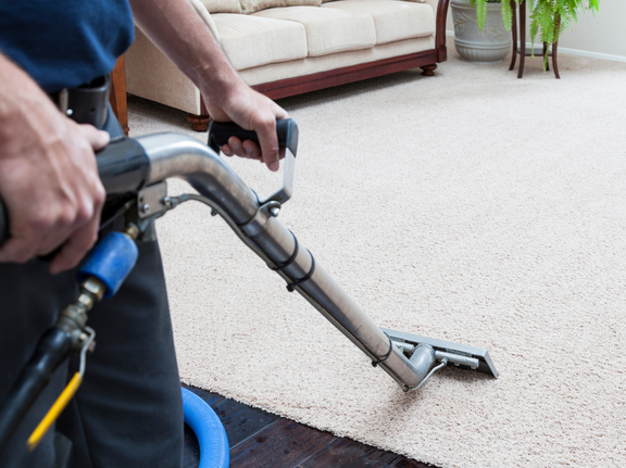 This is a photo of a man with a steam cleaner cleaning a cream carpet. 